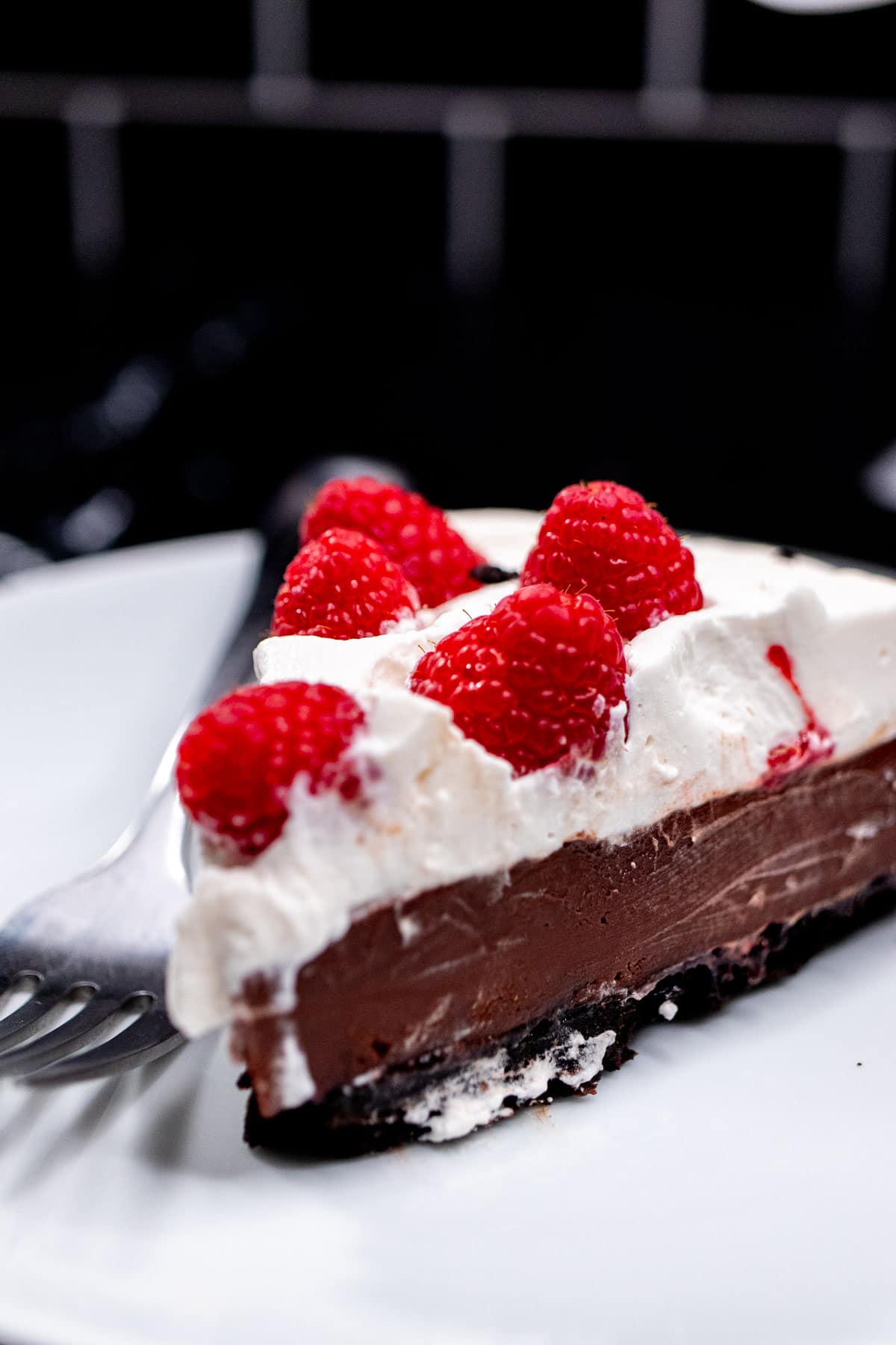 A slice of chocolate raspberry pie topped with whipped cream and fresh raspberries on a plate.
