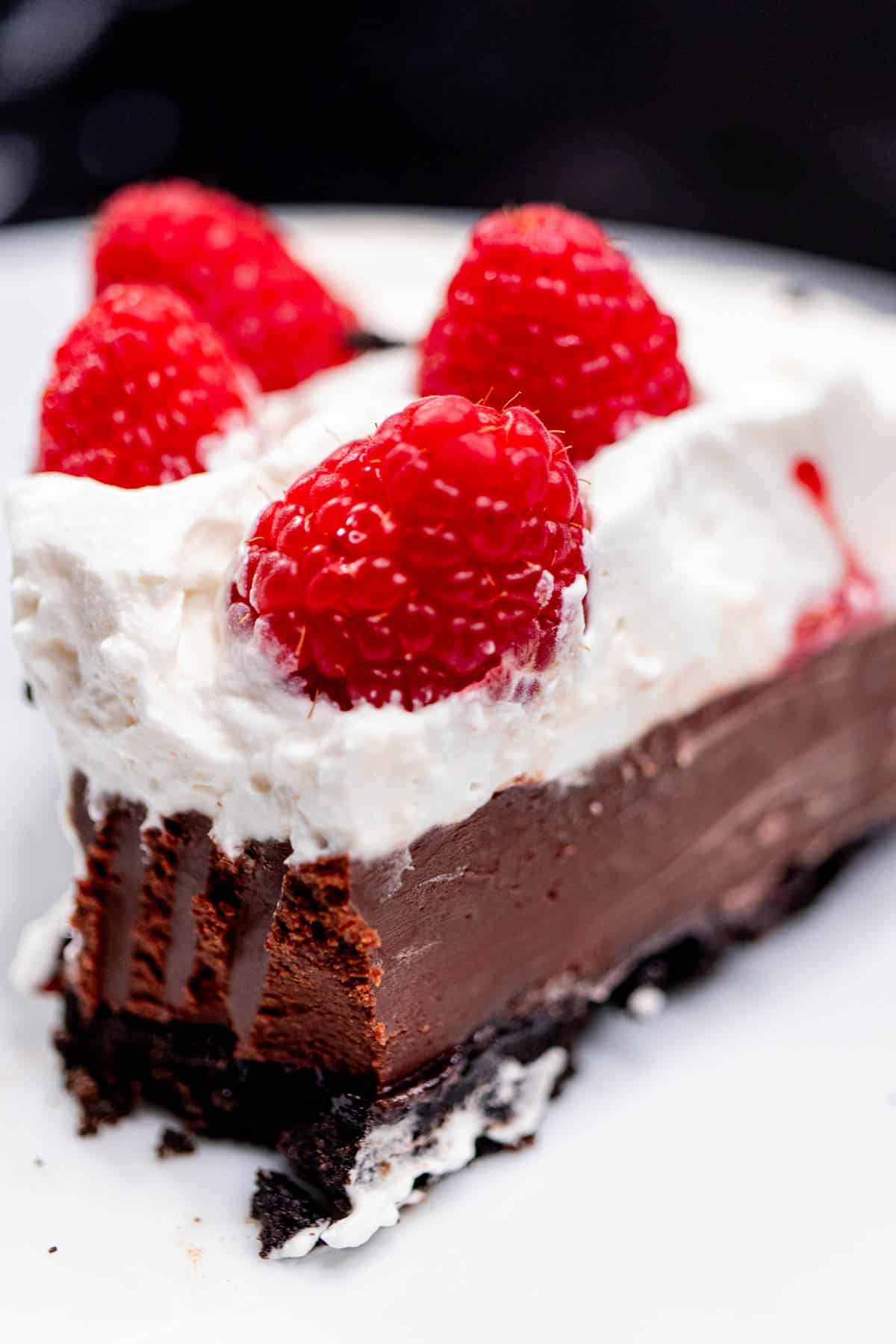 Close up view of a slice of chocolate raspberry tart with whipped cream with a bit missing.
