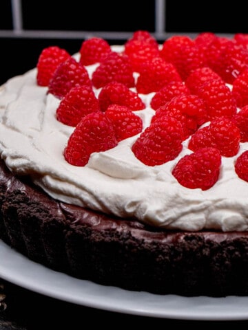 A chocolate raspberry tart topped with whipped cream and fresh raspberries on a white plate.