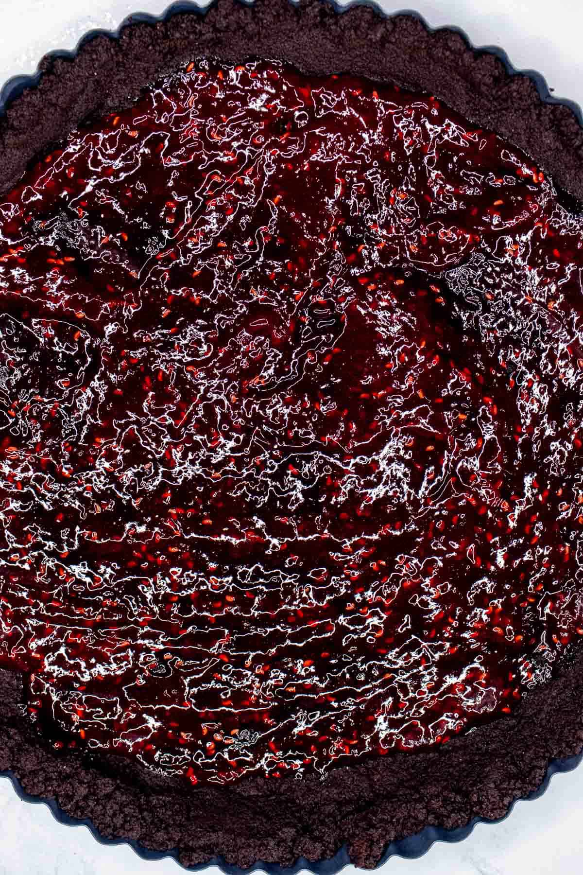 Raspberry preserves coating the bottom of a chocolate tart.