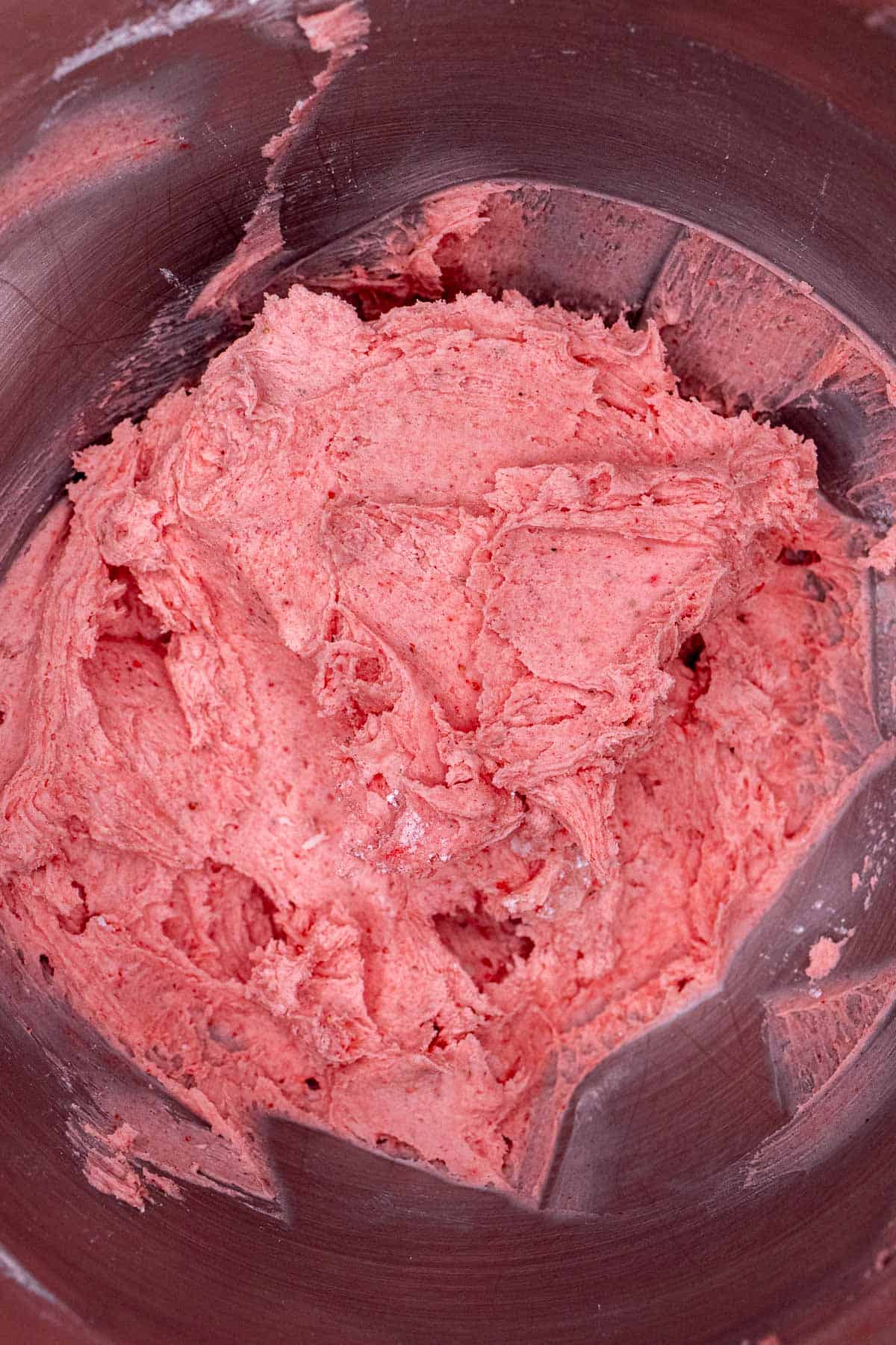 Strawberry buttercream in bowl of stand mixer after being mixed with everything but cream.
