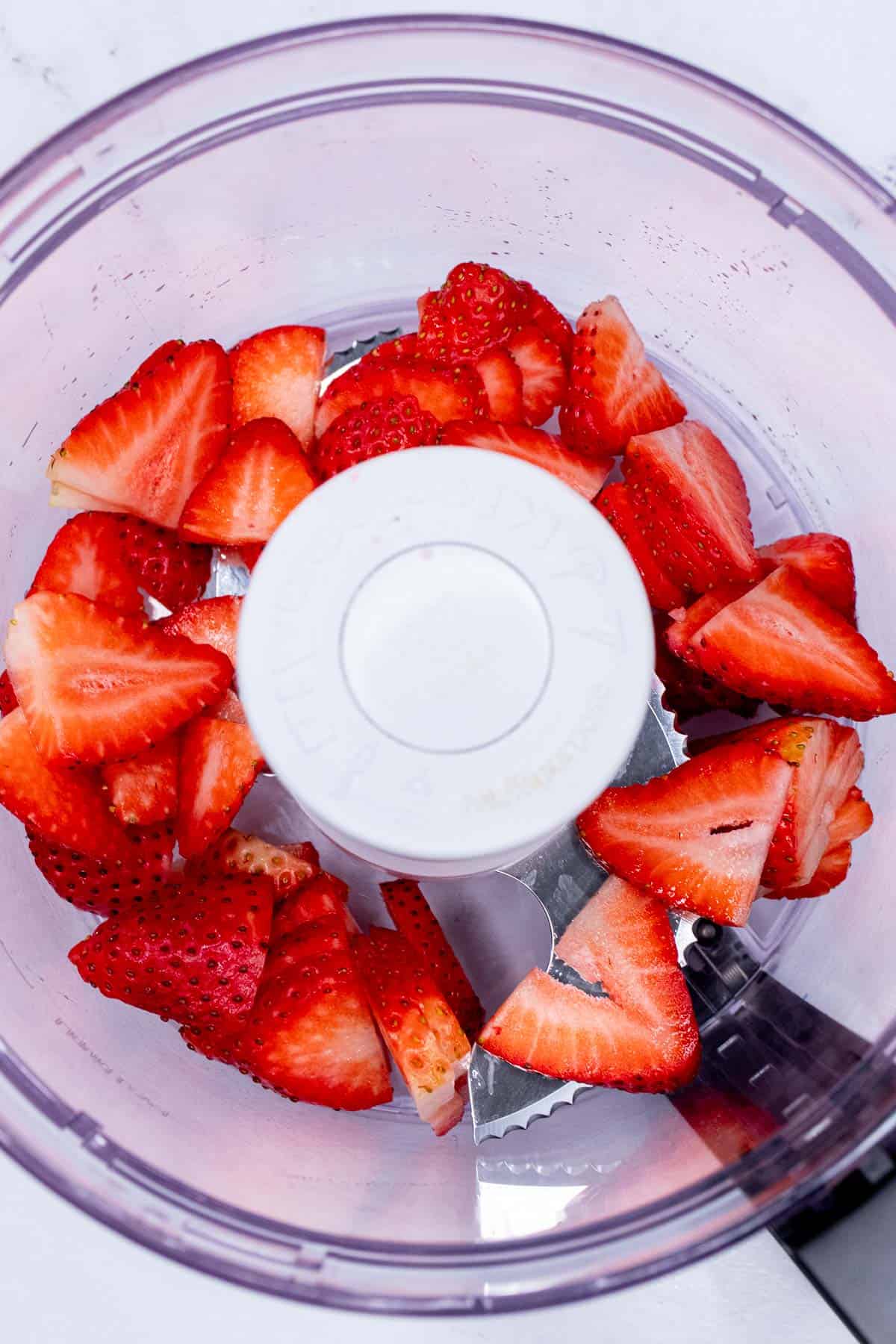 Adding sliced strawberries to a food processor. 