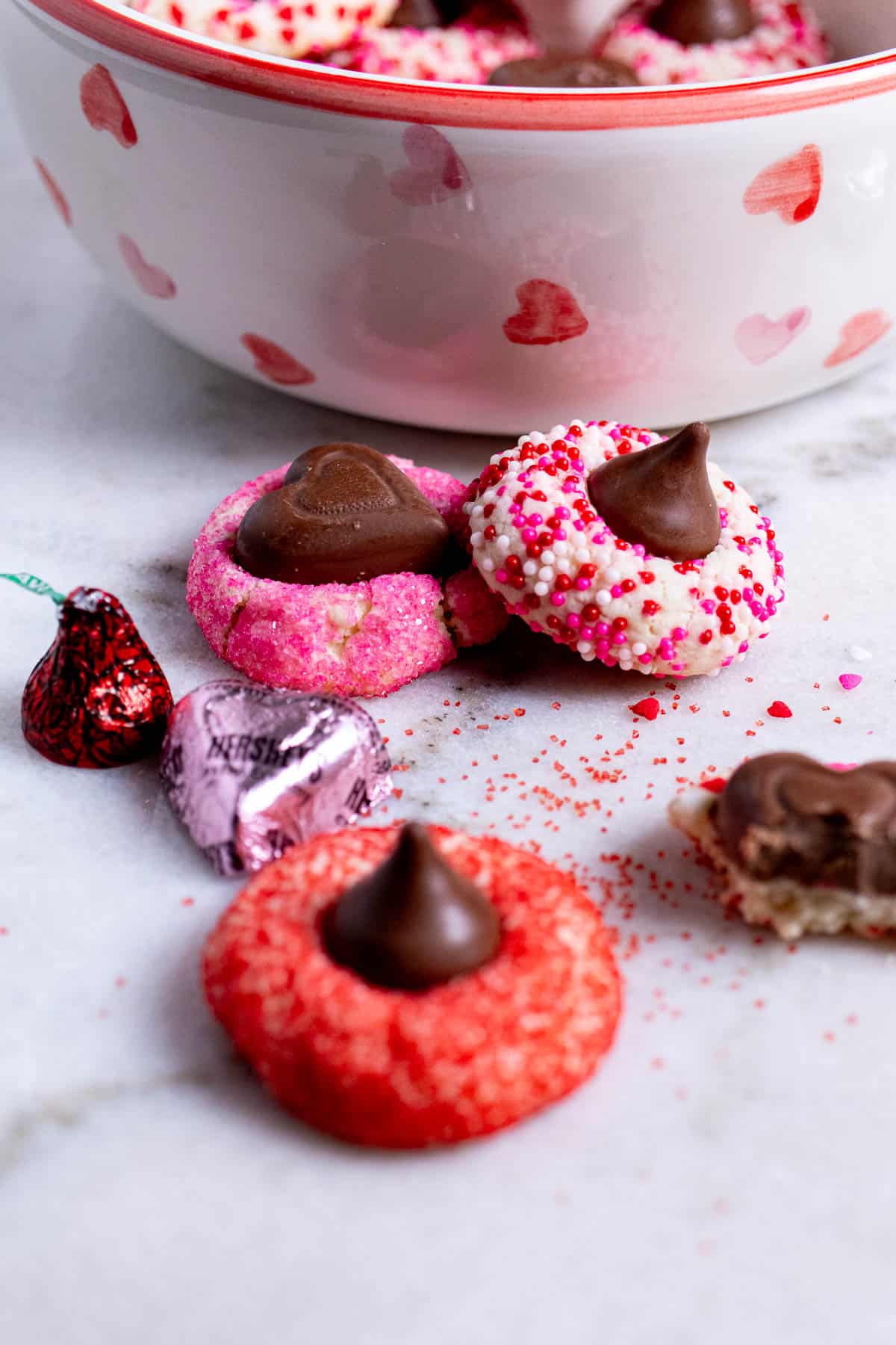 A red Valentine heart blossom cookie on marble with a pink and sprinkle covered one behind it.