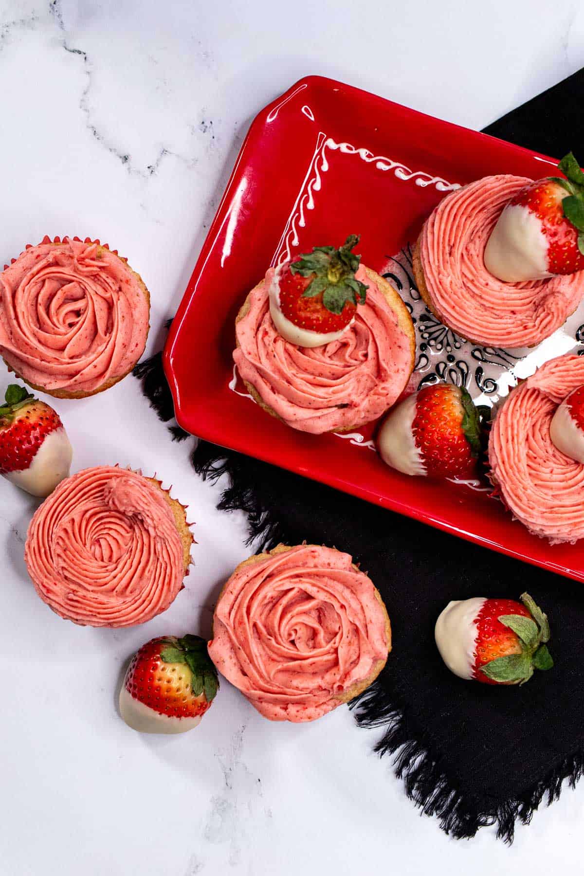 Overhead view of white chocolate strawberry cupcakes topped with strawberry buttercream rosettes and white chocolate dipped strawberries.
