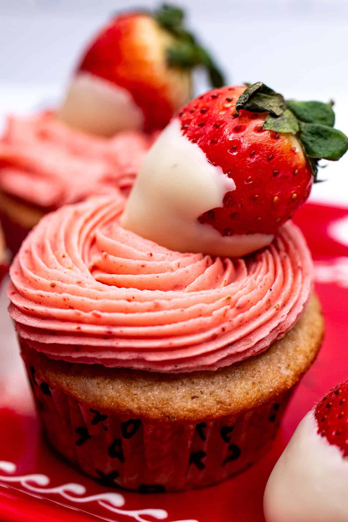 Close up of a white chocolate strawberry cupcake topped with strawberry buttercream and a strawberry dipped in white chocolate.