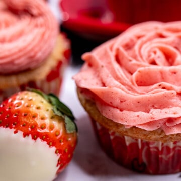 White chocolate strawberry cupcake topped with strawberry buttercream and a strawberry dipped in white chocolate next to it.