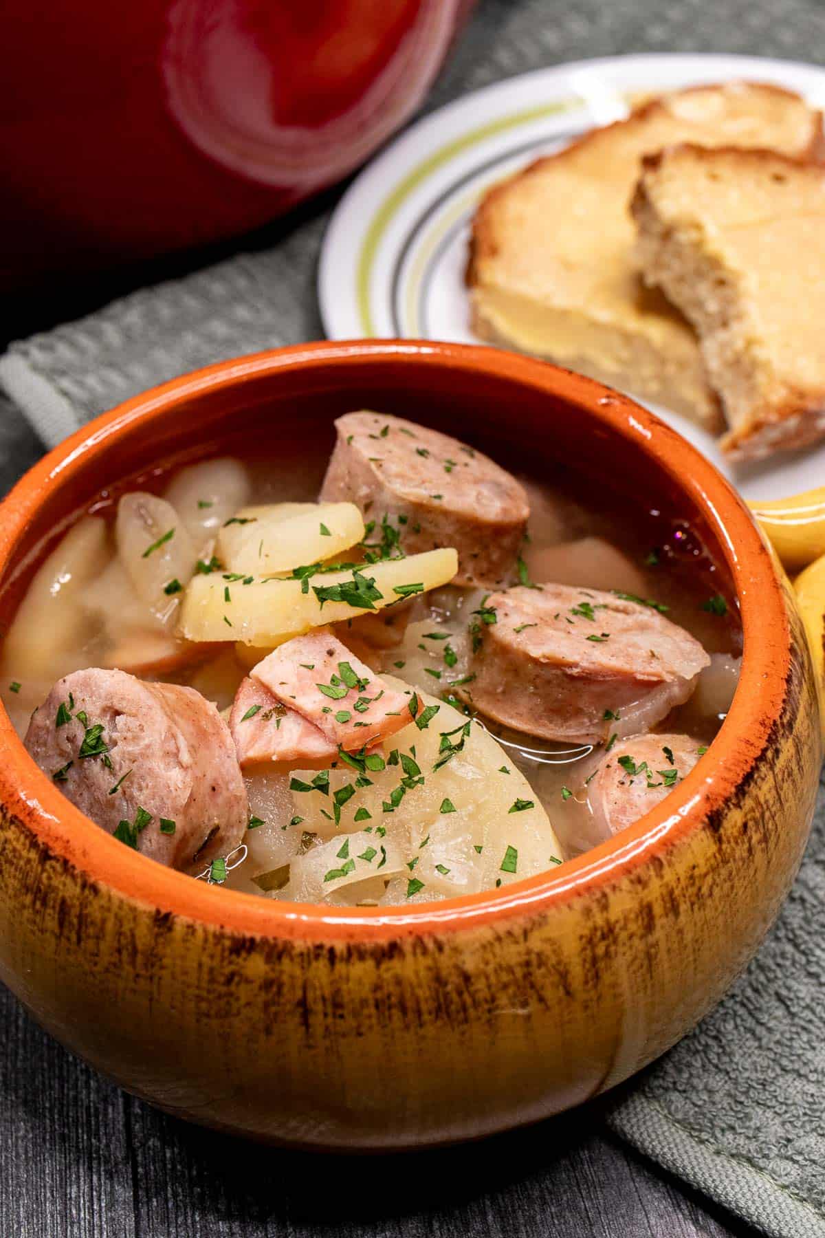 A bowl of Dublin coddle with sliced of Irish soda bread on a plate behind it.