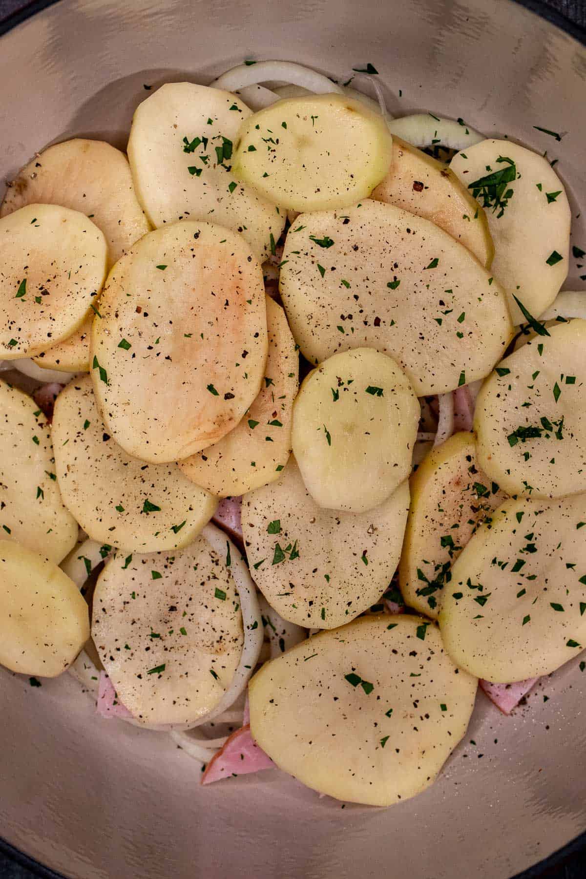 Adding sliced potatoes to the coddle above the onions.