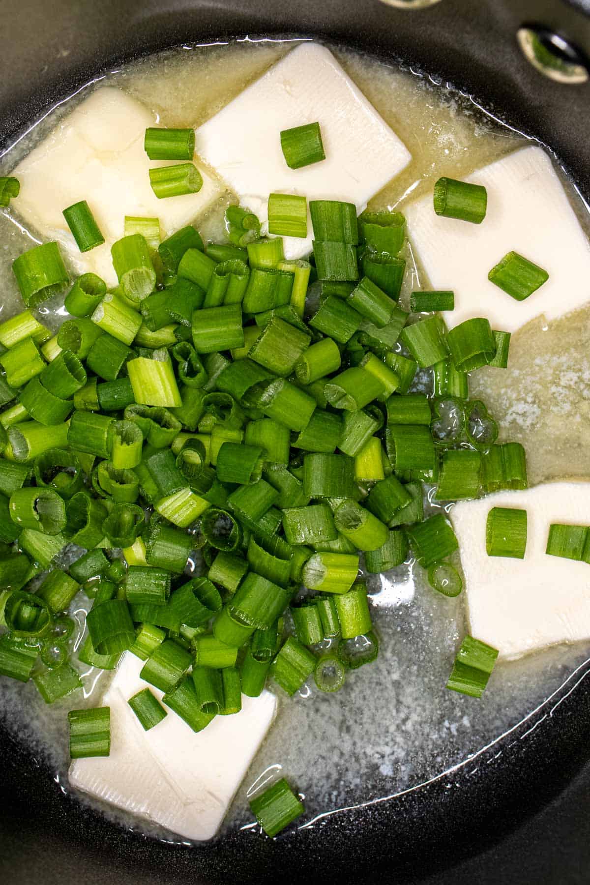 Butter melting in a skillet with chopped spring onions.