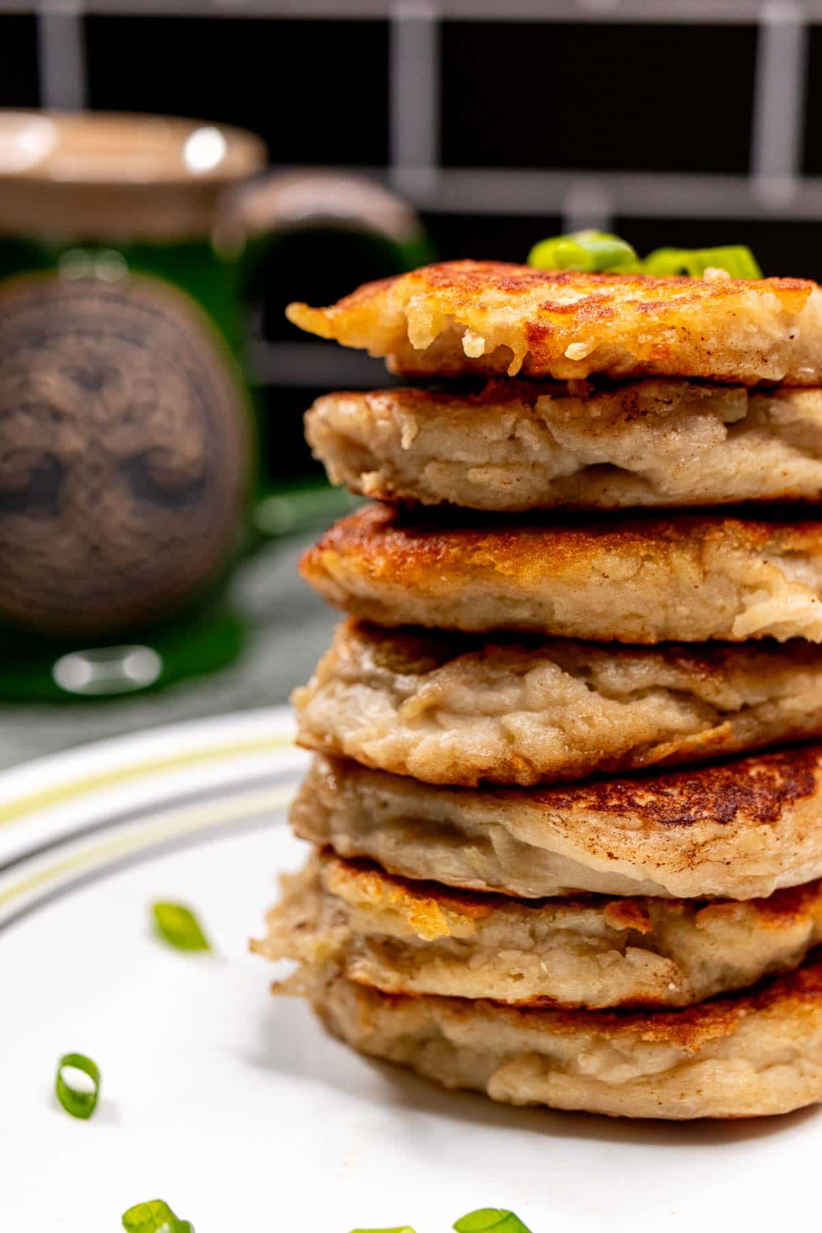 Seven boxty potato pancakes stacked on top of one another on a plate, with a green Irish teacup behind  them.