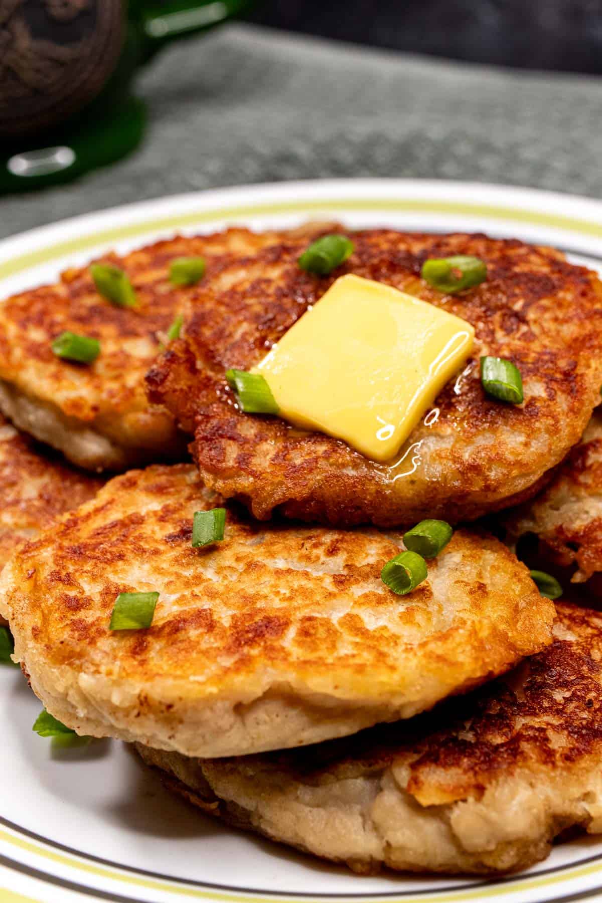 Plate of Irish potato pancakes topped with butter and chopped spring onion.