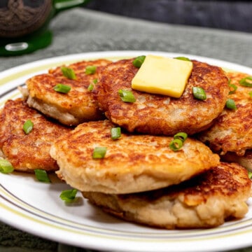 Irish boxty potato pancakes served on a plate and topped with butter and chopped green onions.