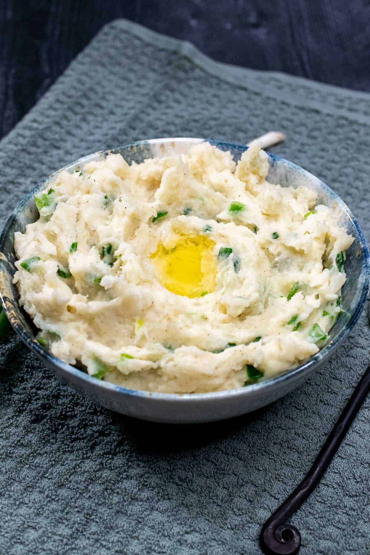 A bowl of Irish champ, creamy mashed potatoes with green onions, with melted butter pooling in the middle.