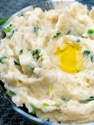 A bowl of Irish champ, creamy mashed potatoes with green onions, with melted butter pooling in the middle.