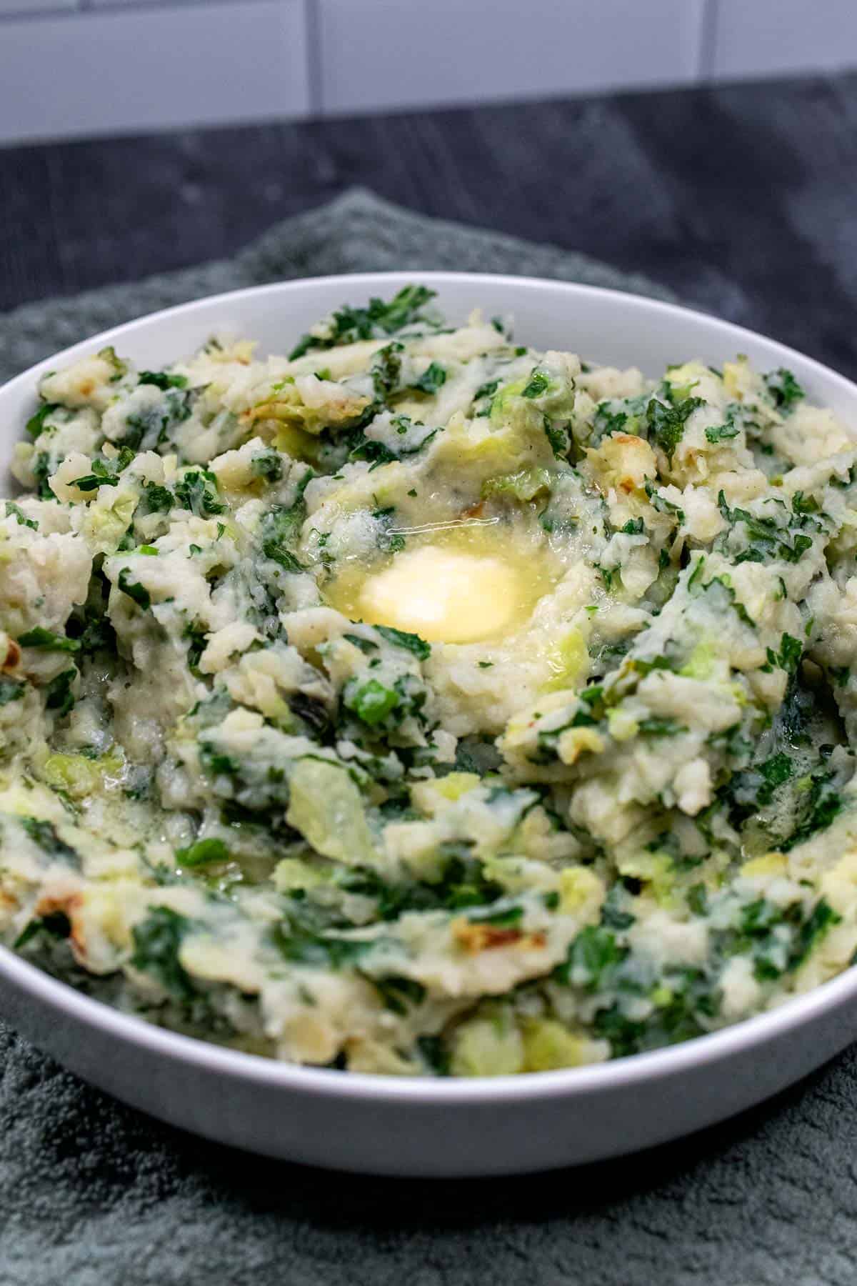 A large, white bowl of Irish colcannon with a pool of butter on top.