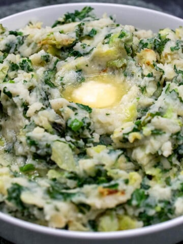 A large white bowl filled with traditional Irish colcannon and melted butter pooling in the center.