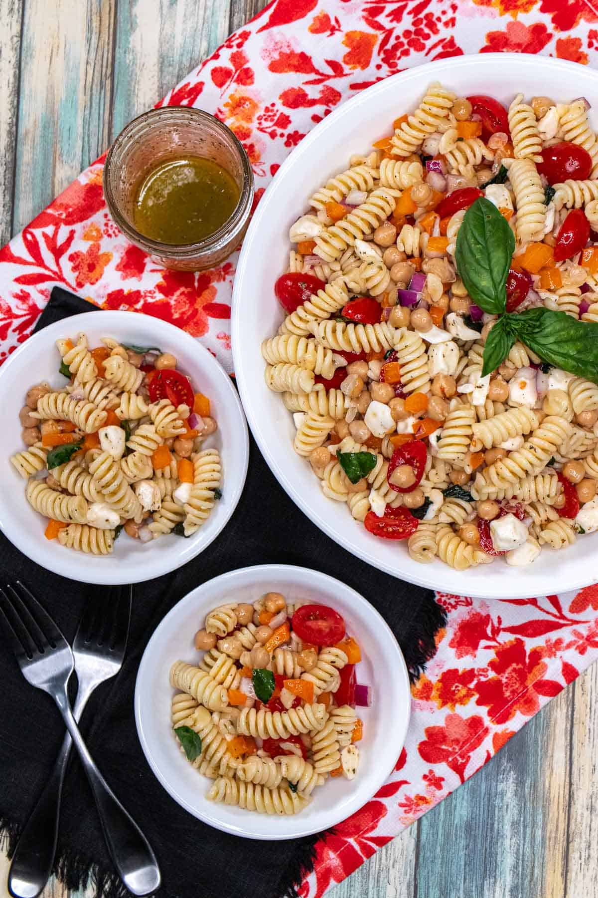 Overhead view of a large bowl of cold pasta salad with two side bowls filled with some next to it.