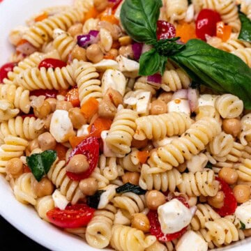 Large bowl of easy pasta salad without mayo. Made with tomatoes, mozzarella, onion, pepper, basil, and chickpeas.