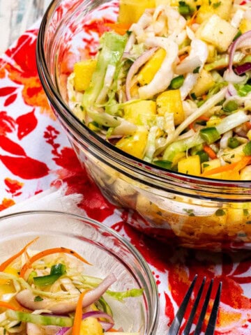 A large glass bowl with pineapple coleslaw with a small side dish of it next to the larger bowl.