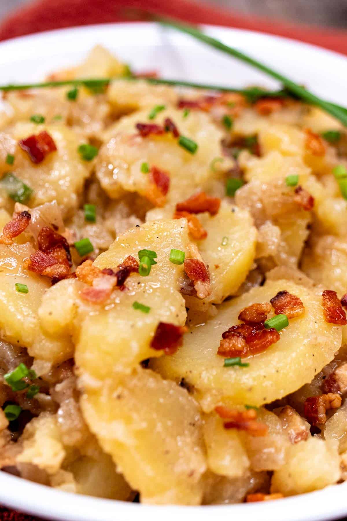 Bavarian potato salad in a serving bowl topped with bacon and chives.