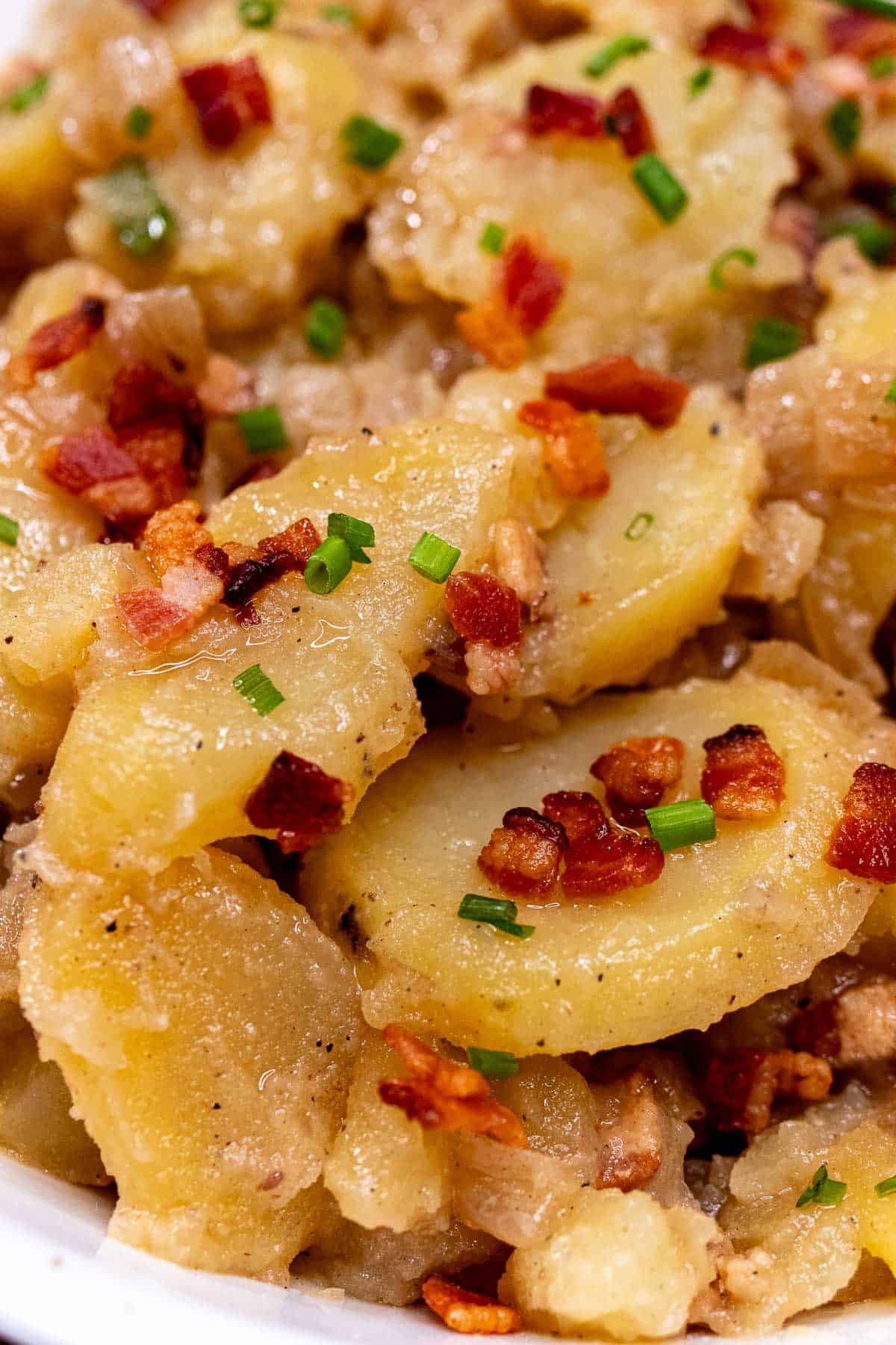 Close up view of Bavarian potato salad topped with bacon bits and chives.