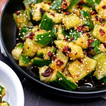 A black bowl filled with smashed cucumber salad tossed with chili crisp.