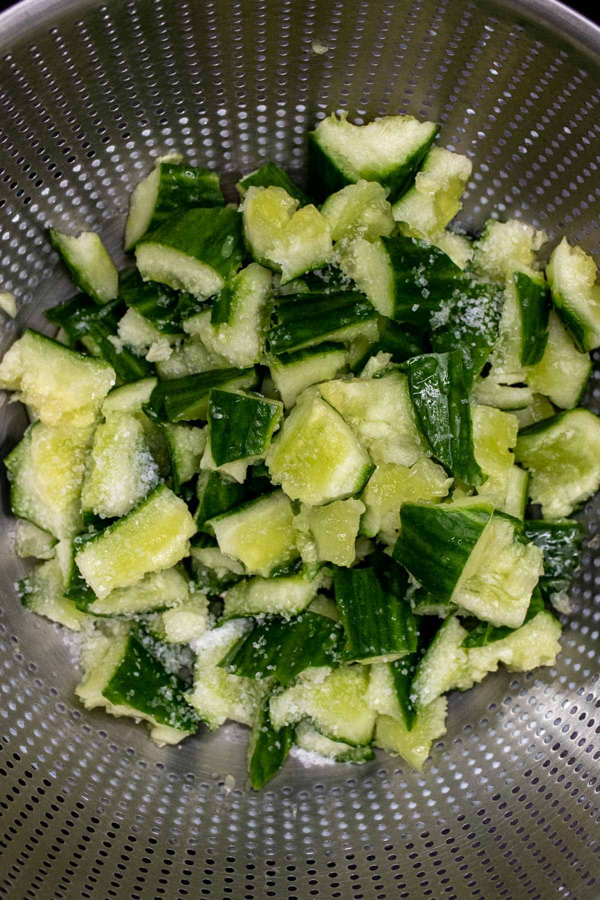 Smashed and torn apart cucumber pieces tossed with salt and draining in a colander.