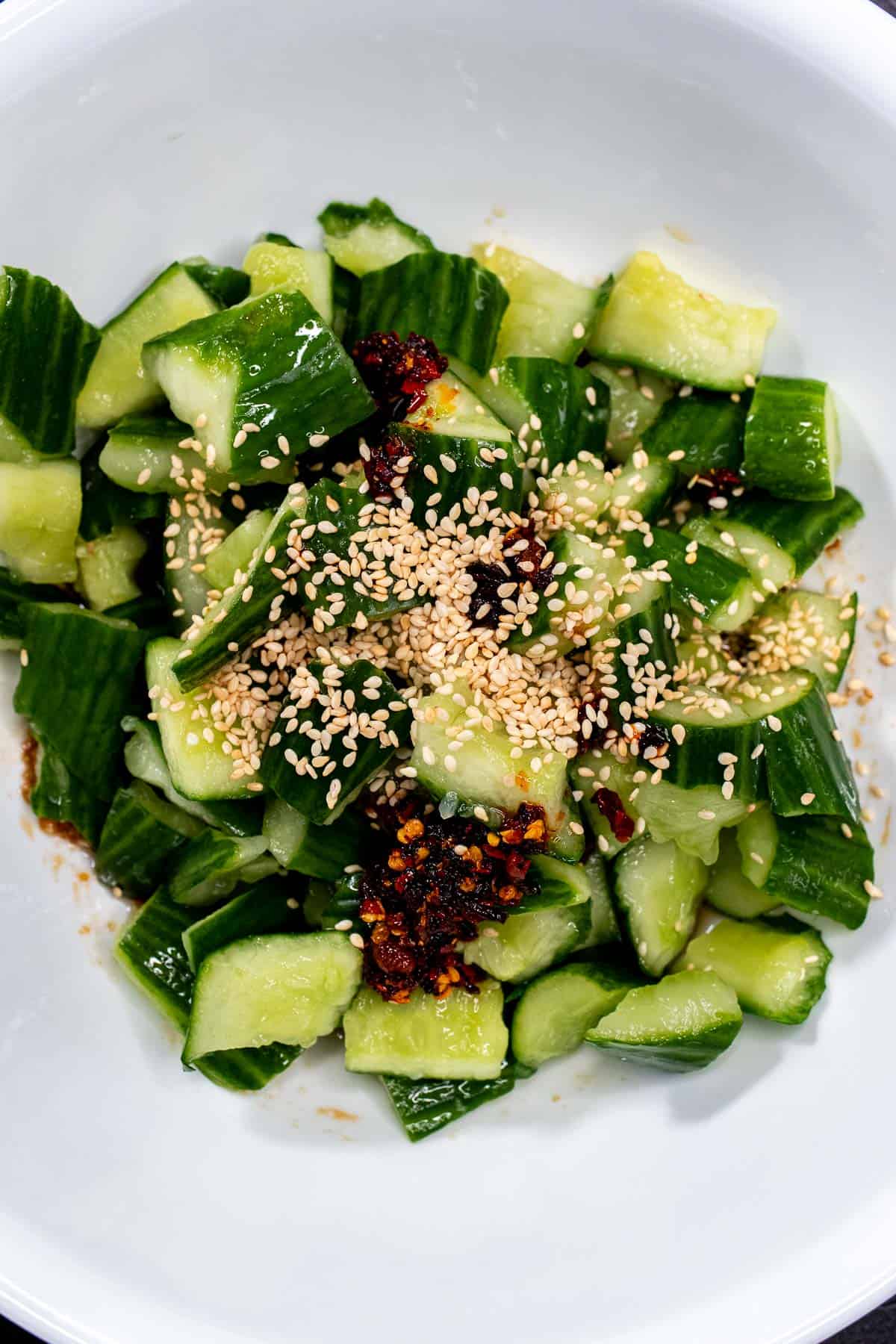 Smashed cucumbers tossed with dressing in a mixing bowl.