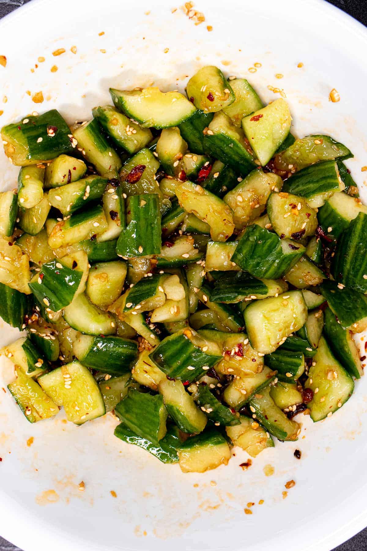 Chinese smashed cucumbers tossed with dressing, sesame seeds, and chili crisp in a mixing bowl.