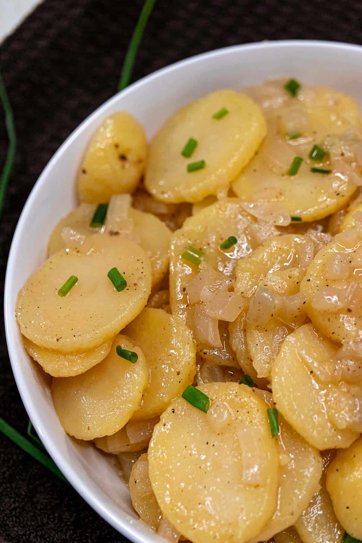 A serving bowl filled with sliced, marinated potatoes for southern German potato salad.