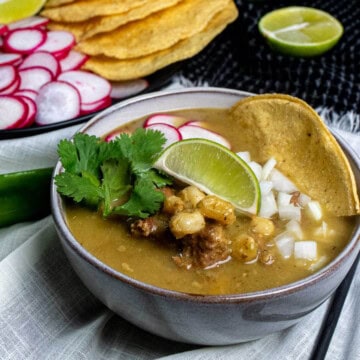 New Mexican style pork pozole verde with Hatch chiles, topped with radishes, onion, cilantro, and a tostado in a bowl.