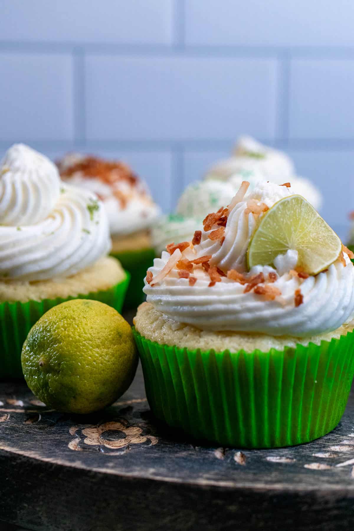 Key lime coconut cupcakes with piped cream cheese frosting on top with various toppings.