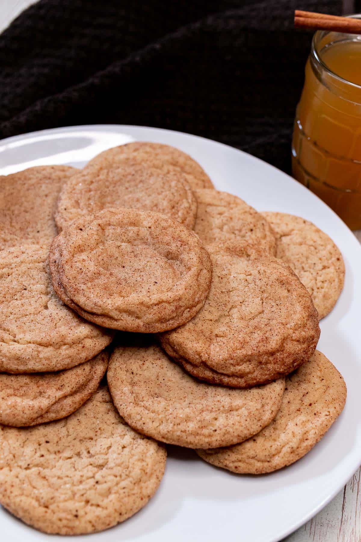 A plate full of apple cider snickerdoodles with a glass of hot apple cider.