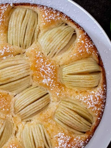 A whole German sunken apple cake topped with thinly sliced apples fanned out and powdered sugar.