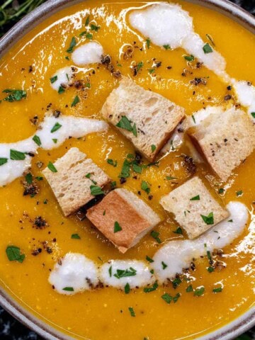 A bowl of creamy roasted carrot soup topped with croutons and coconut cream.