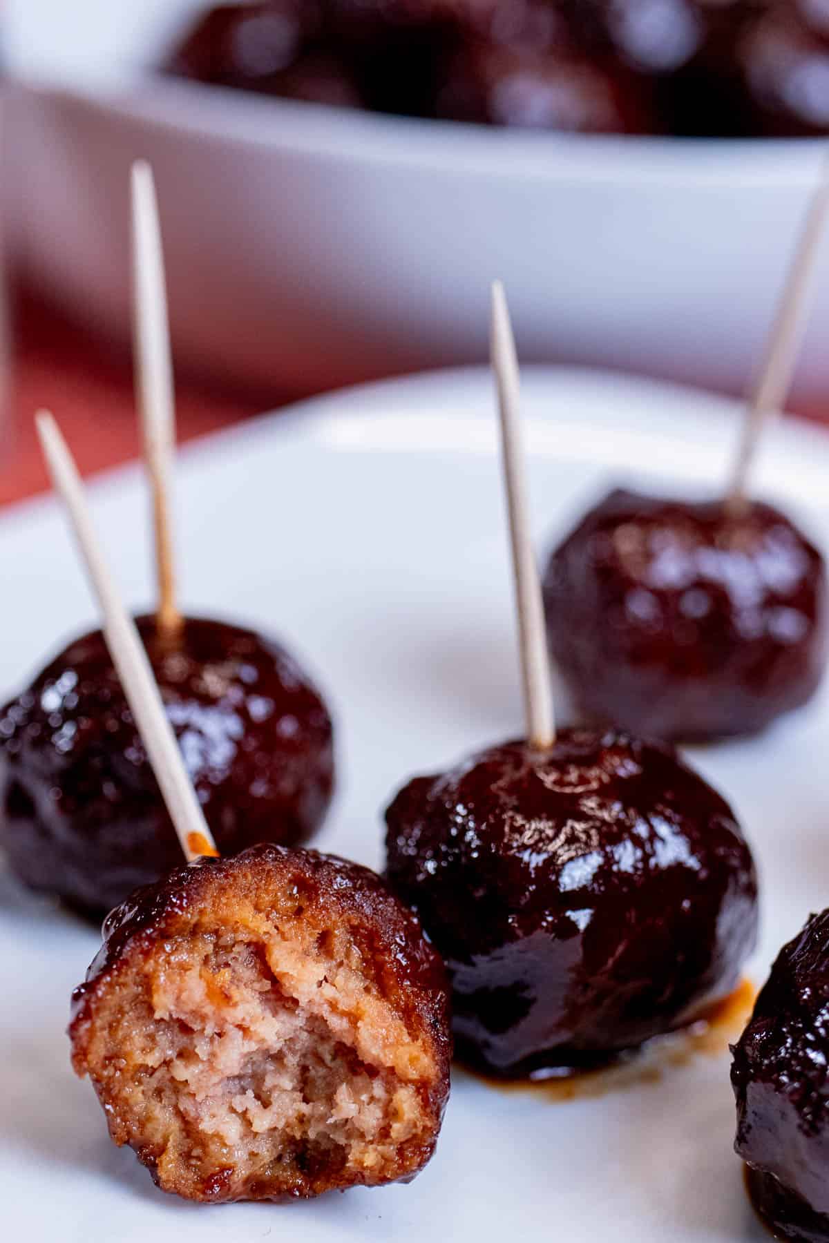 An appetizer plate with tooth picked blackberry chipotle BBQ meatballs on it with a bite taken out of one.