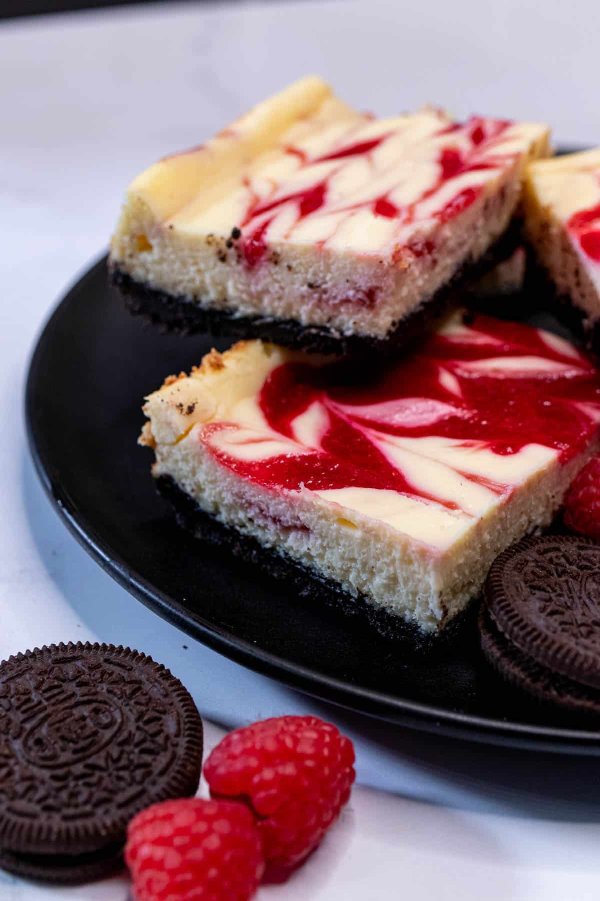 A plate of white chocolate raspberry cheesecake bars with Oreos and raspberries.