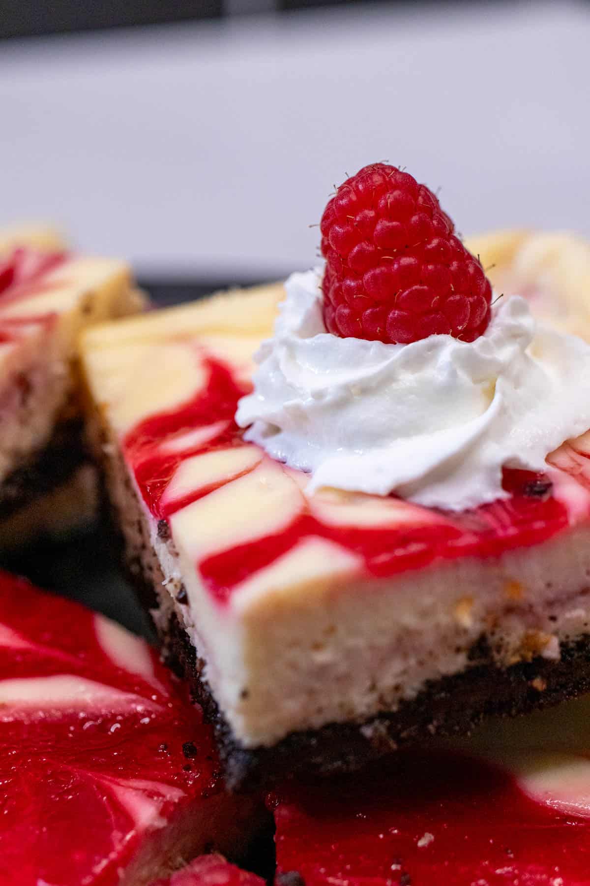 A white chocolate raspberry cheesecake bar topped with whipped cream and a fresh raspberry.