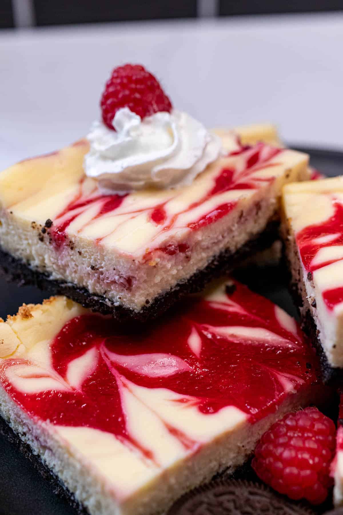 A plate of raspberry cheesecake bars with some topped with whipped cream and raspberries.
