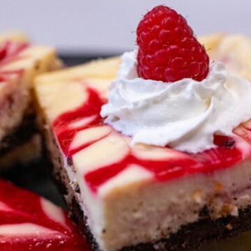 A white chocolate raspberry cheesecake bar topped with whipped cream and a fresh raspberry.