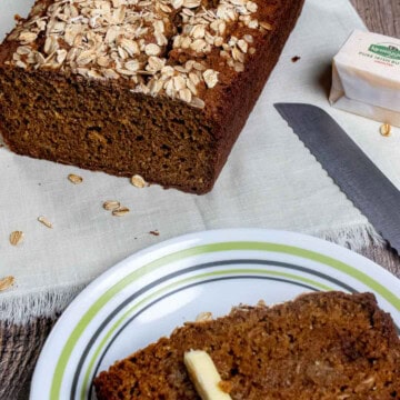 A buttered slice of Guinness brown bread on a plate with the loaf behind it.