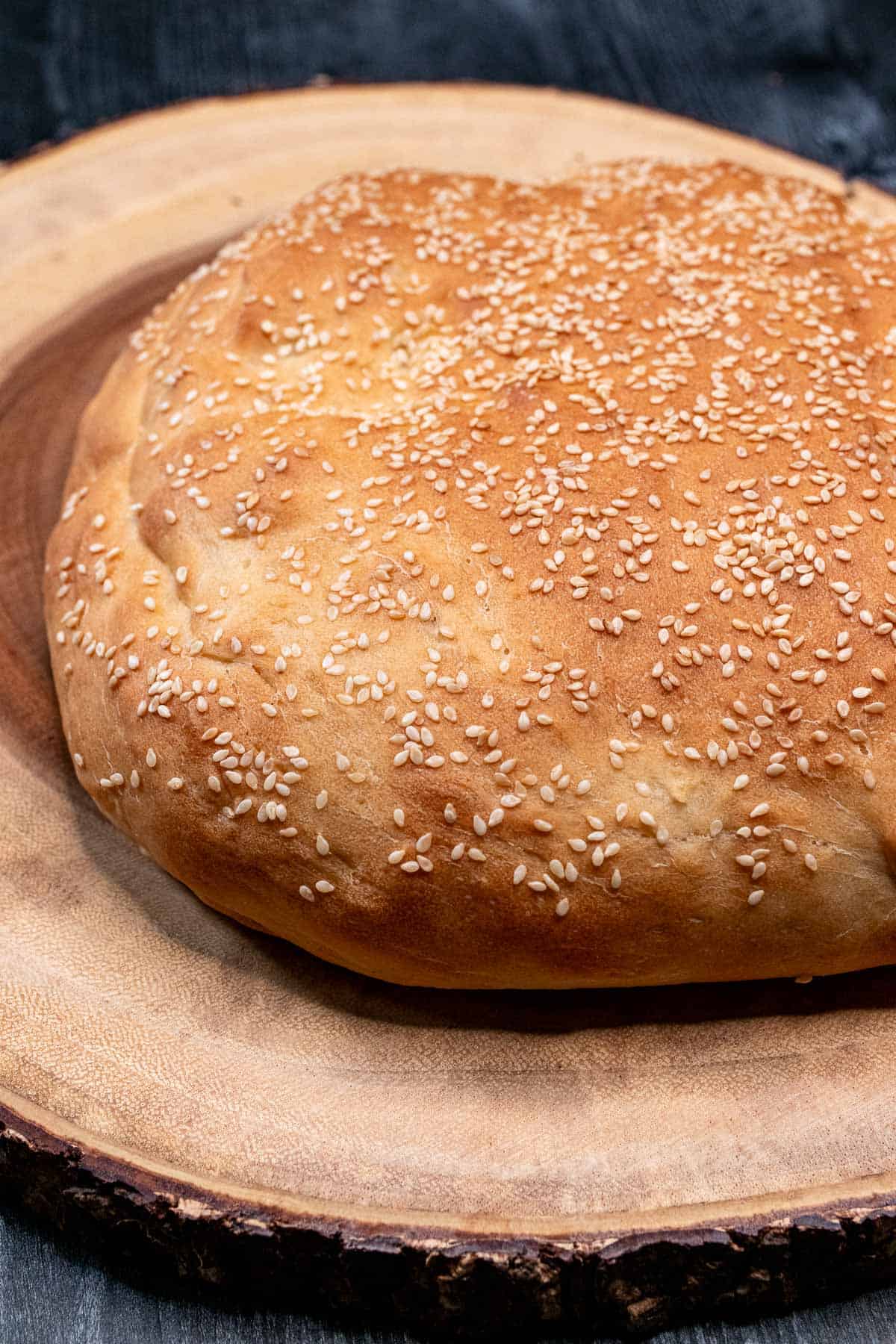 Unsliced homemade muffuletta bread on a wooden tray.