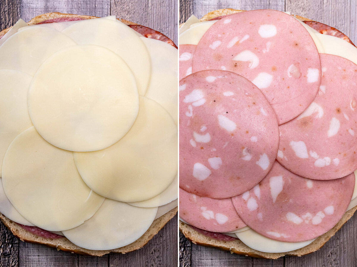 Layering on the rest of the meat and cheese to a New Orleans muffaletta sandwich.