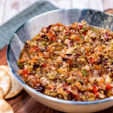 An olive salad in a large bowl, served with assorted crackers.