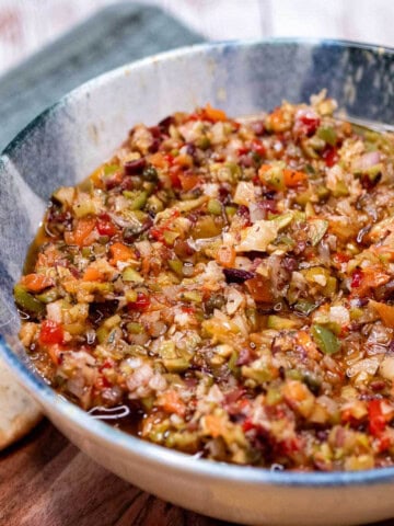 An olive salad in a large bowl, served with assorted crackers.