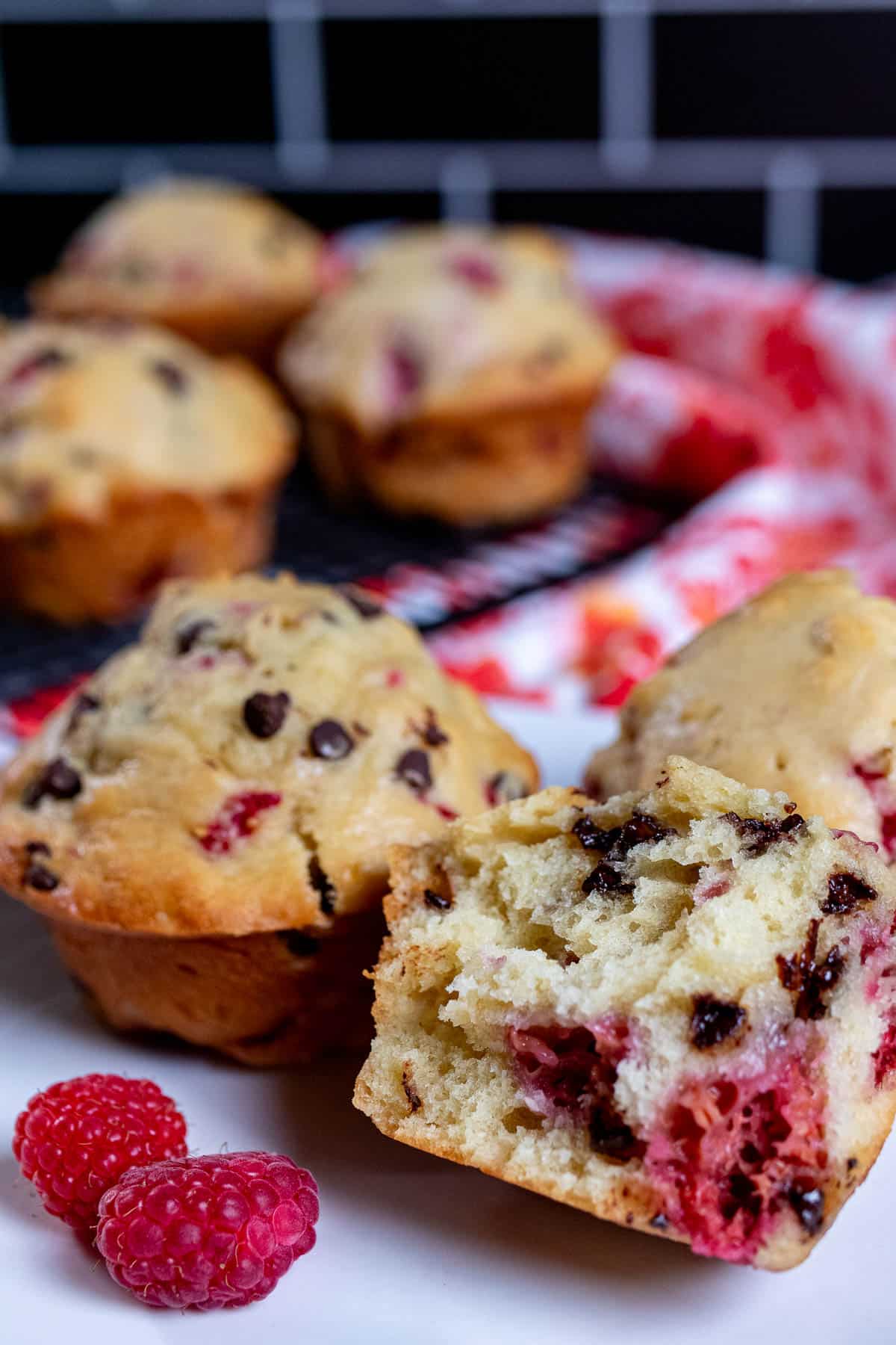 Raspberry chocolate chip muffins on a cooling rack and a plate, with one torn open.