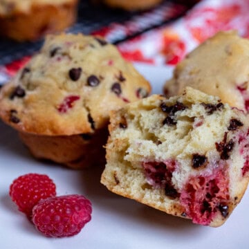 A plate of raspberry chocolate chip muffins with one torn open next to fresh raspberries.