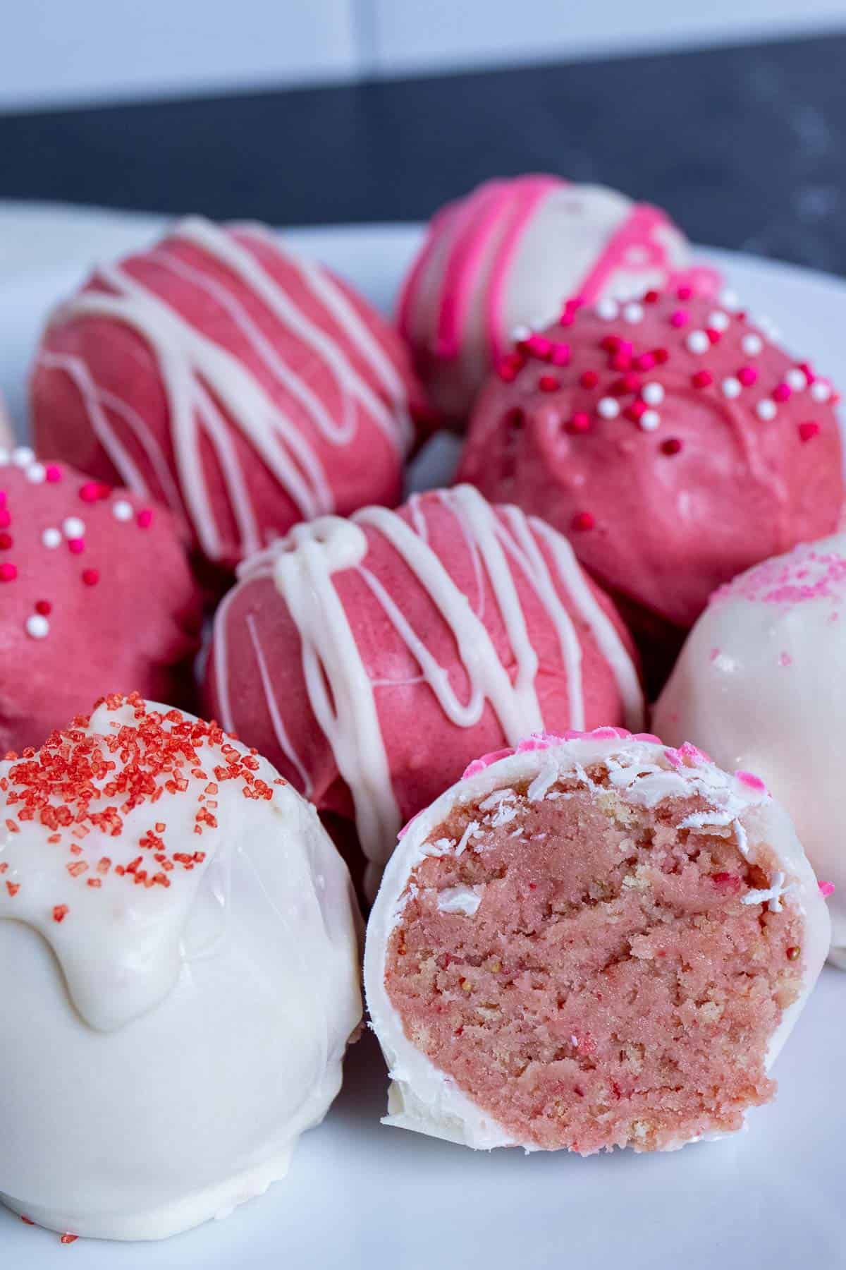 A plate of decorated strawberry Oreo truffles with one cut in half.