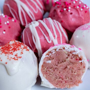 A plate of decorated strawberry Oreo truffles with one cut in half.