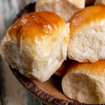 A wooden serving bowl full of honey butter yeast rolls with honey buttered tops.